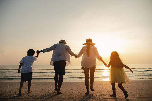 Happy asian family are having fun on a tropical beach in sunset.Parent and children playing together on beach.Happy family travel on beach in holiday,Summer and vacations concept.