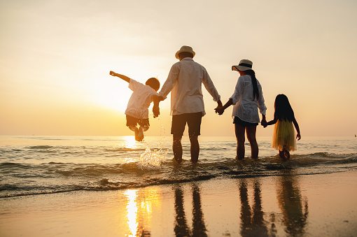 Happy asian family jumping together on the beach in holiday. Silhouette of the family holding hands enjoying the sunset on the  beach.Happy family and vacations concept.