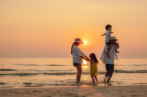 glückliche asiatische familie, die während der sommerferien strandaktivitäten genießt. eltern und kinder genießen den sonnenuntergang am strand. urlaubsreisekonzept, sommerferien. - holding men casual mother stock-fotos und bilder