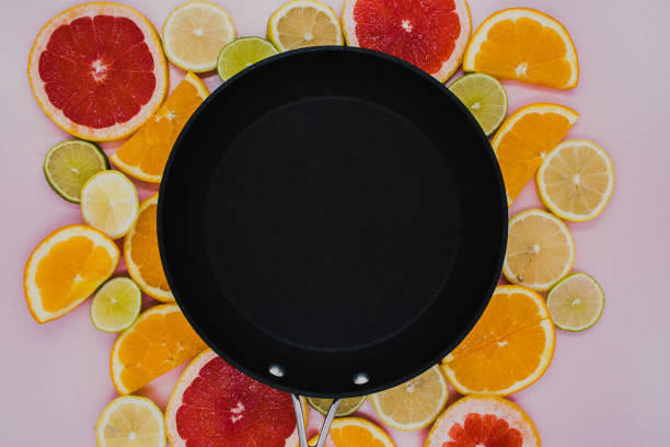 Black frying pan on sliced citrus plants. Oranges, grapefruit, lemon, lime on a pink background. flat lay