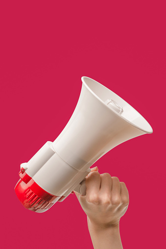Megaphone in woman hands on a viva magenta background.  Copy space.