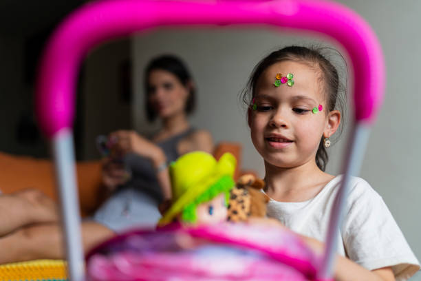 Latina girl, 8 years old, playing in the living room of her house, with her dolls, while behind her is her mother watching the cell phone