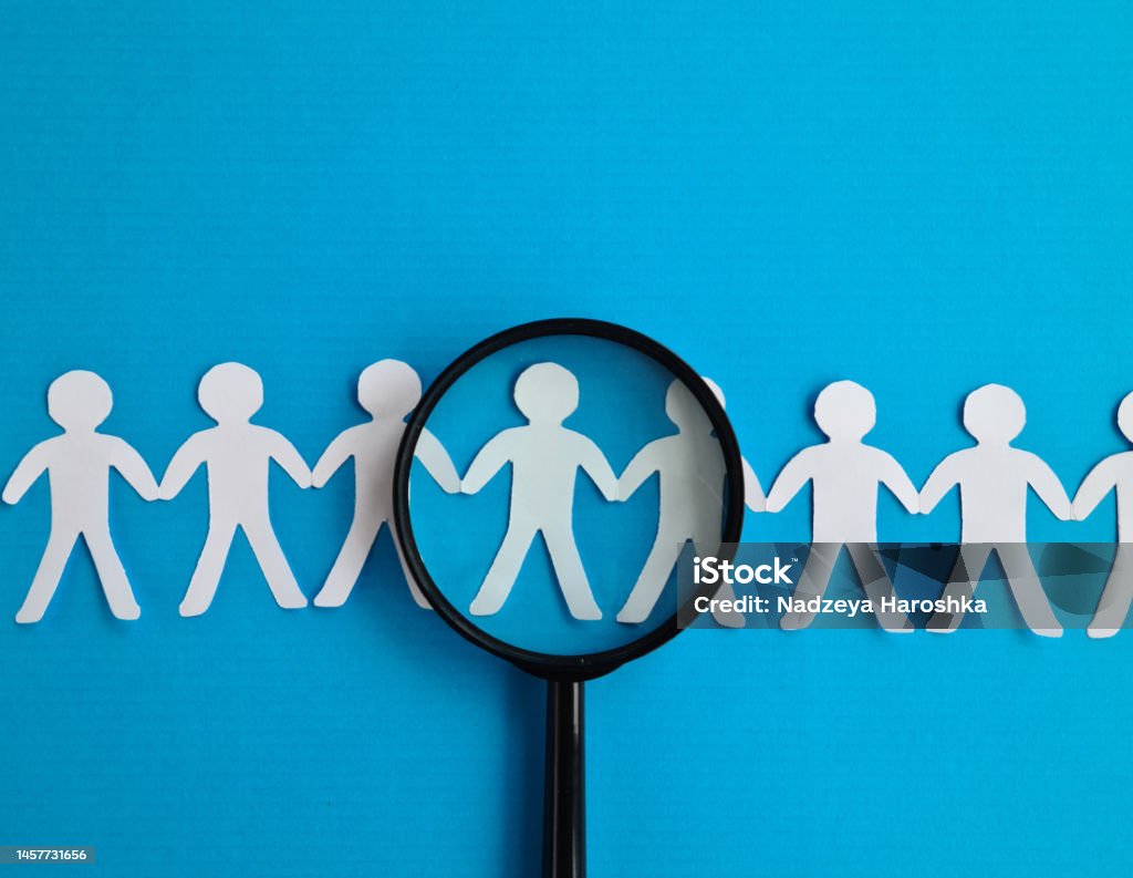 Abstract paper figures of people under black magnifying glass on a blue background Abstract paper figures of people under black magnifying glass on a blue background. Concept of hiring Recruitment Stock Photo