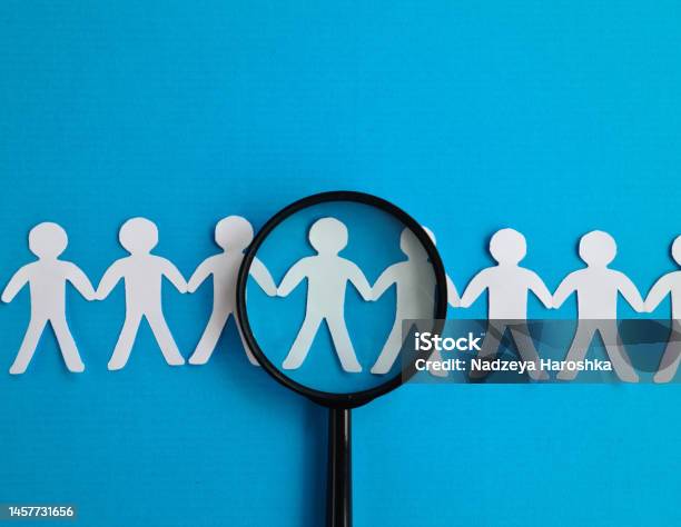 Abstract Paper Figures Of People Under Black Magnifying Glass On A Blue Background Stock Photo - Download Image Now