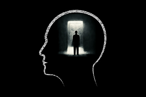 Human head with silhouette of a businessman looking towards a bright doorway in dark room