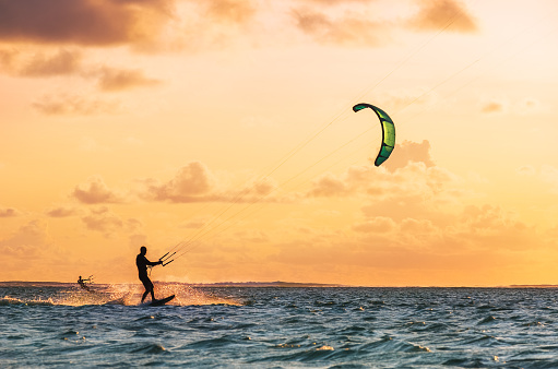 Sunset sky over the Indian Ocean bay with a two kiteboarders riding kiteboards with a green bright power kites. Active sport people and beauty in Nature concept image. Le Morne beach, Mauritius.