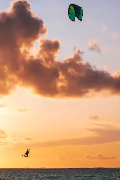 Photo of Sunset sky over the Indian Ocean bay with kiteboarder jumping trick on kiteboard with a green bright power kite. Active sport people and beauty in Nature concept image. Le Morne beach, Mauritius.