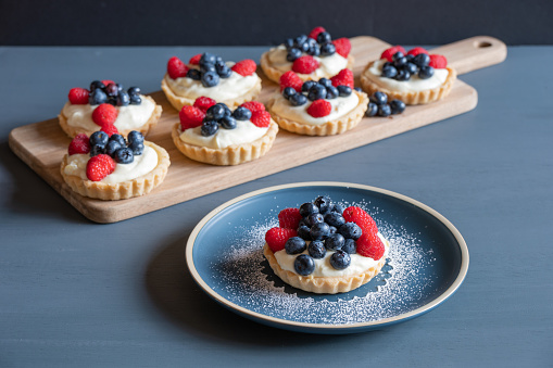 Raspberry and blueberry tarts on a blue table against a grey background.