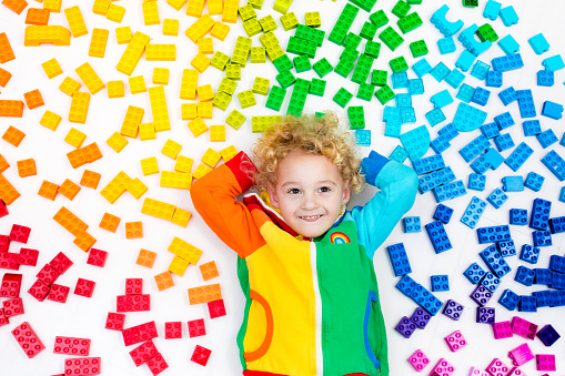 Funny little boy playing with colorful rainbow plastic blocks. Kids play, create and learn colors. Educational toys for creative children. Preschooler building block toys. Kid playing on the floor.