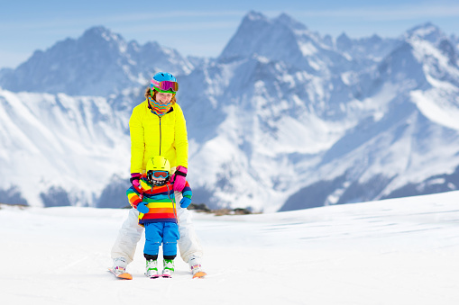 Family ski vacation. Group of skiers in Swiss Alps mountains. Mother and child skiing in winter. Parents teach kids alpine downhill skiing. Ski gear and wear, safe helmets.