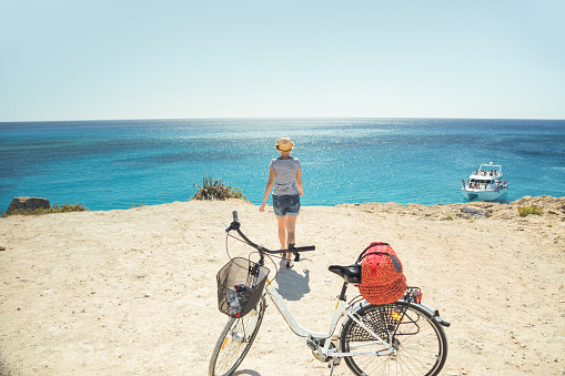 Young caucasian woman riding a bike during sunny day by the sea. Summer vacation concept. Mediterranean islands