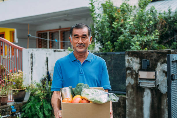 Smiling Asian male volunteer holding a cardboard box of food and drink at the food bank stock photo