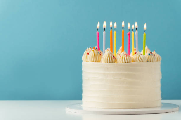 istock Birthday cake with white cream cheese frosting decorated with multicolored lit candles on a blue background. Happy Birthday concept. Tradition of making a wish while blowing out candles on a cake 1457738426