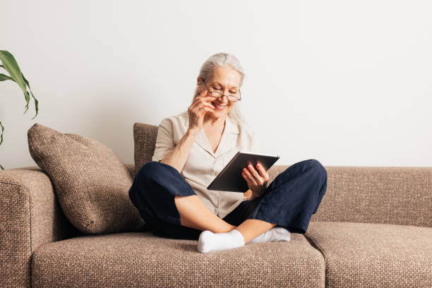 istock Smiling senior woman in eyeglasses sitting on a couch with a digital tablet 1457741507