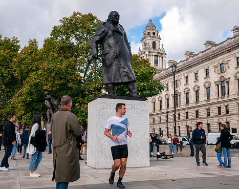 Tourists in Parliament Square, Westminster, beside the bronze statue of the former British Prime Minister, Sir Winston Churchill. In the background is another bronze statue of another former Prime Minister, David Lloyd-George.