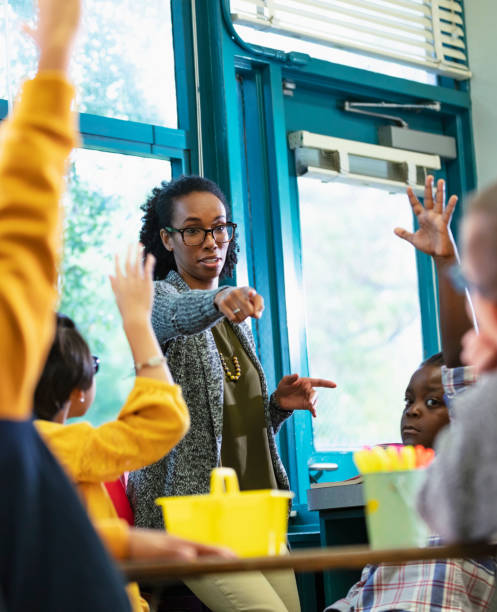 Teacher in classroom points to student raising hand stock photo