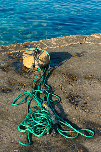 Stone mooring and ropes on a concrete jetty, next to the sea