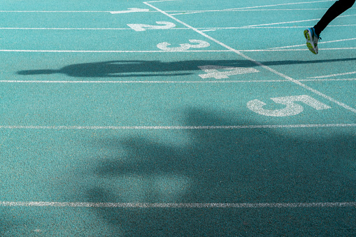 running track starting line background photo. only the legs of the runner are in the frame. numbers appear on the starting line. Shot with a full-frame camera in daylight.