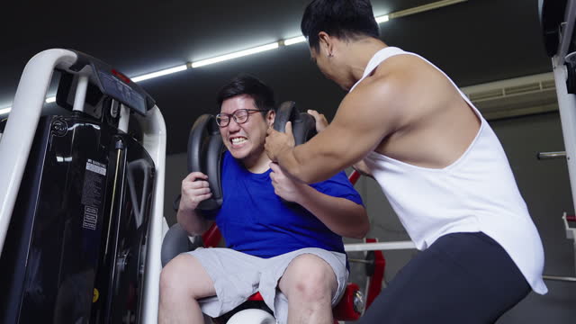 Young large build Asian man gave his all out on exercising his abdominal muscle by using the ab crunch machine with support from his fitness trainer at the gym