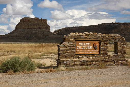 Clouds shadow Fajada Butte in the background with the Chaco Culture National Historical Park southern entrance sign in the foreground.