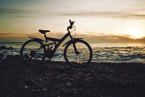 Mountain bike stands on a pebble beach in the evening yellow sunset, back sunlight, focus on foreground