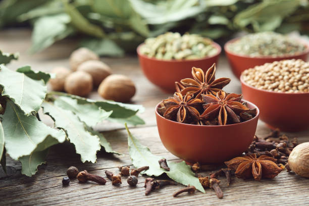 Bowl of anise stars. Bowls of aromatic spices - coriander, cardamom pods on background. Gloves, laurel leaves, nutmeg on table. Ingredients for healthy cooking. Ayurveda remedies. stock photo