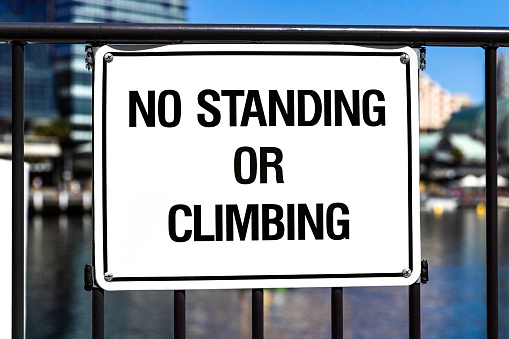 Sign NO STANDING OR CLIMBING on fence in city, background with copy space, full frame horizontal composition