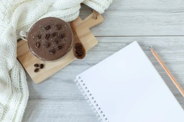 Spiral notebook with blank page, wooden pencil, and cup of coffee on table with woolen scarf. Copy space for text. Top view. Writing notes, morning strategy, and goals, planning concept.