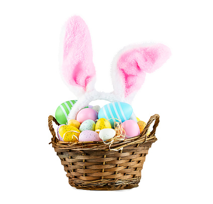 Basket with colorful Easter eggs and pink bunny ears isolated on white