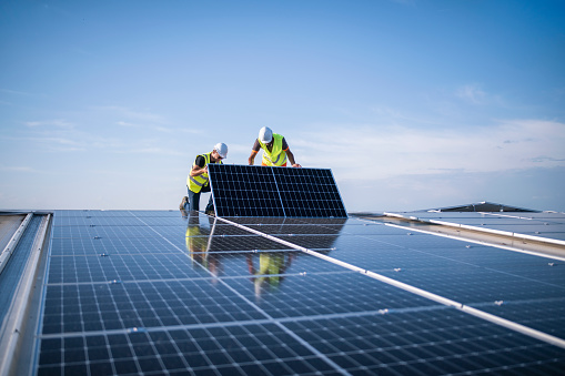 Team of two engineers installing solar panels on industrial factory roof.