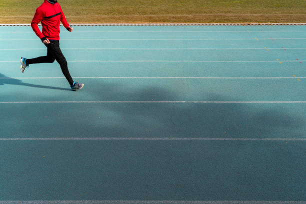 young man doing sports on the running track. young man wearing red and black tracksuit running on public sports ground. Taken with a full-frame camera in daylight