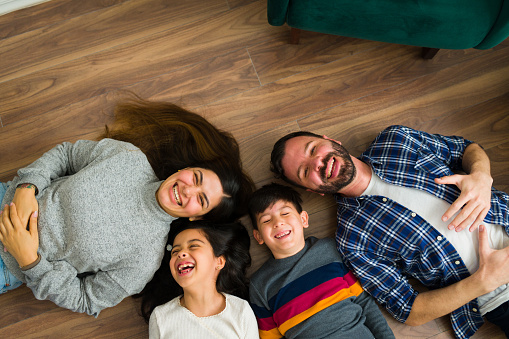 Top view of a happy family laughing with their happy children and having fun relaxing on the floor at home