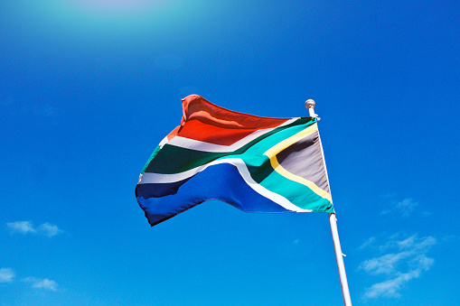 South African flag flies in a strong wind against a mostly clear summer sky.