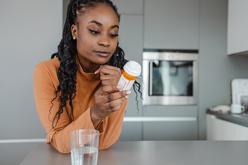Photo of a woman leaning on a kitchen counter and reading instructions for medicine