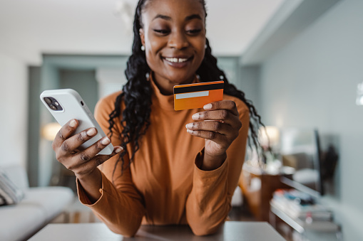 Smiling African-American woman using smart phone for online banking while holding a credit card