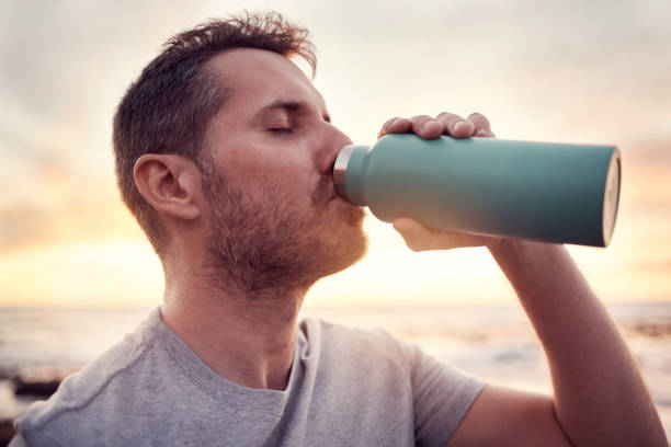 mężczyzna, fitness i butelka wody z tłem plaży o zachodzie słońca dla pragnienia, nawodnienia i zdrowego stylu życia na świeżym powietrzu do ćwiczeń, treningu i treningu. sportowiec pijący orzeźwienie w naturze - drinking men water bottle zdjęcia i obrazy z banku zdjęć