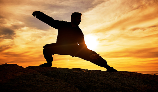 Man, meditation and silhouette, training and tai chi outdoor at a beach, wellness and calm with sunset background. Male, dark and shadow with martial arts, workout and meditate for a balance mindset
