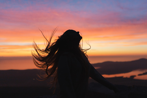 Silhouette of a young woman with long hair. Colorful sunset in the background.