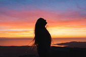 Silhouette of a young woman with long hair during a colorful sunset by the sea