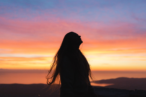Silhouette of a young woman with long hair. Colorful sunset in the background.