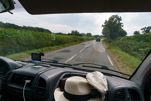 View from passenger seat out of a cockpit of an camper van with dashboard traveling on a road trip on a rural street