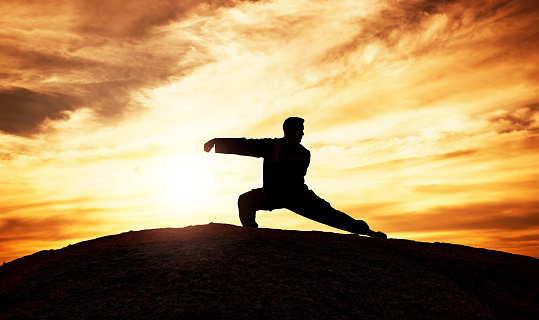 Tai chi, exercise and man at sunset to practice a spiritual workout in nature with an athlete. Silhouette, martial arts training and male fitness practioner doing chi gong on a hill at sunrise