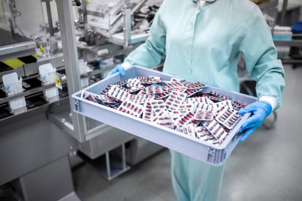 Pharmaceutical Shipping and Logistics A young female worker in protective gear carefully carries a container filled with blister-packaged capsules, a crucial step in the transportation process of pharmaceutical products. Showcasing the importance of safety and attention to detail in the industry. pharmaceutical factory stock pictures, royalty-free photos & images