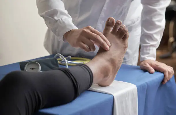 Photo of doctor's hands palpating unrecognizable patient's pedial pulse in the office