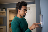 Young man adjusts the temperature at home with a device on the wall