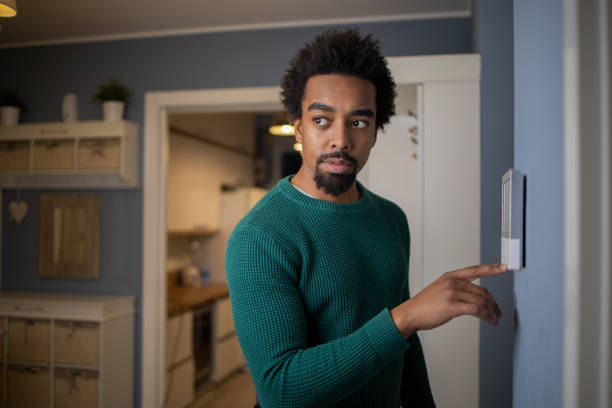 istock Young man adjusts the temperature at home with a device on the wall 1457793826