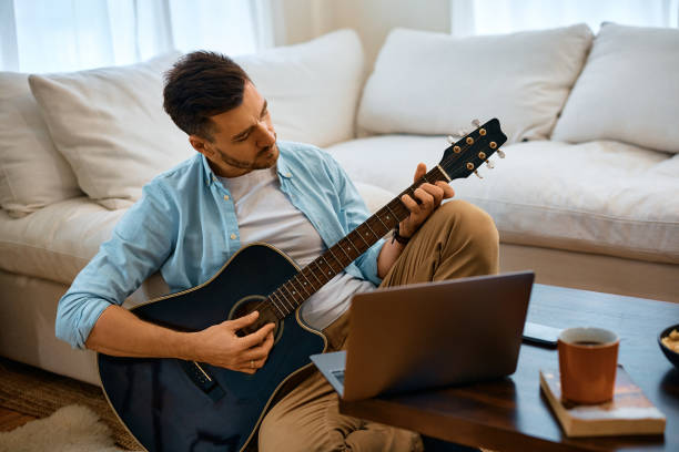 istock Mid adult man playing acoustic guitar while using laptop at home. 1457799334