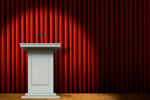 istock White podium on stage under spotlight over red curtain 1457801980