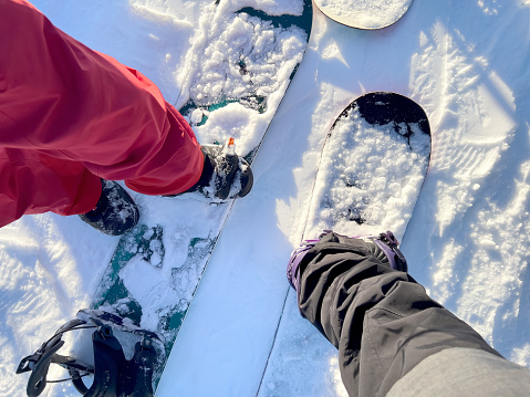Personal perspective looking downwards - Snowboarding friends and family standing in ski lift lineup