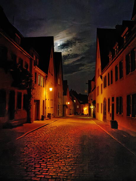 Cobblestone street in Rotherburg Germany bathed in low key street lighting with moonlit clouds overhead